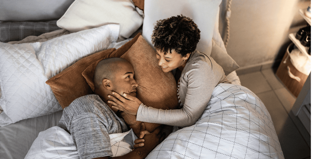 Couple laying in bed with pillows and fluffing bedding