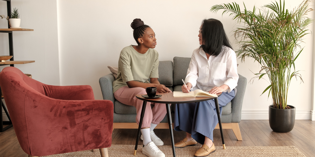 Two women sat on a sofa talking and writing in a notebook