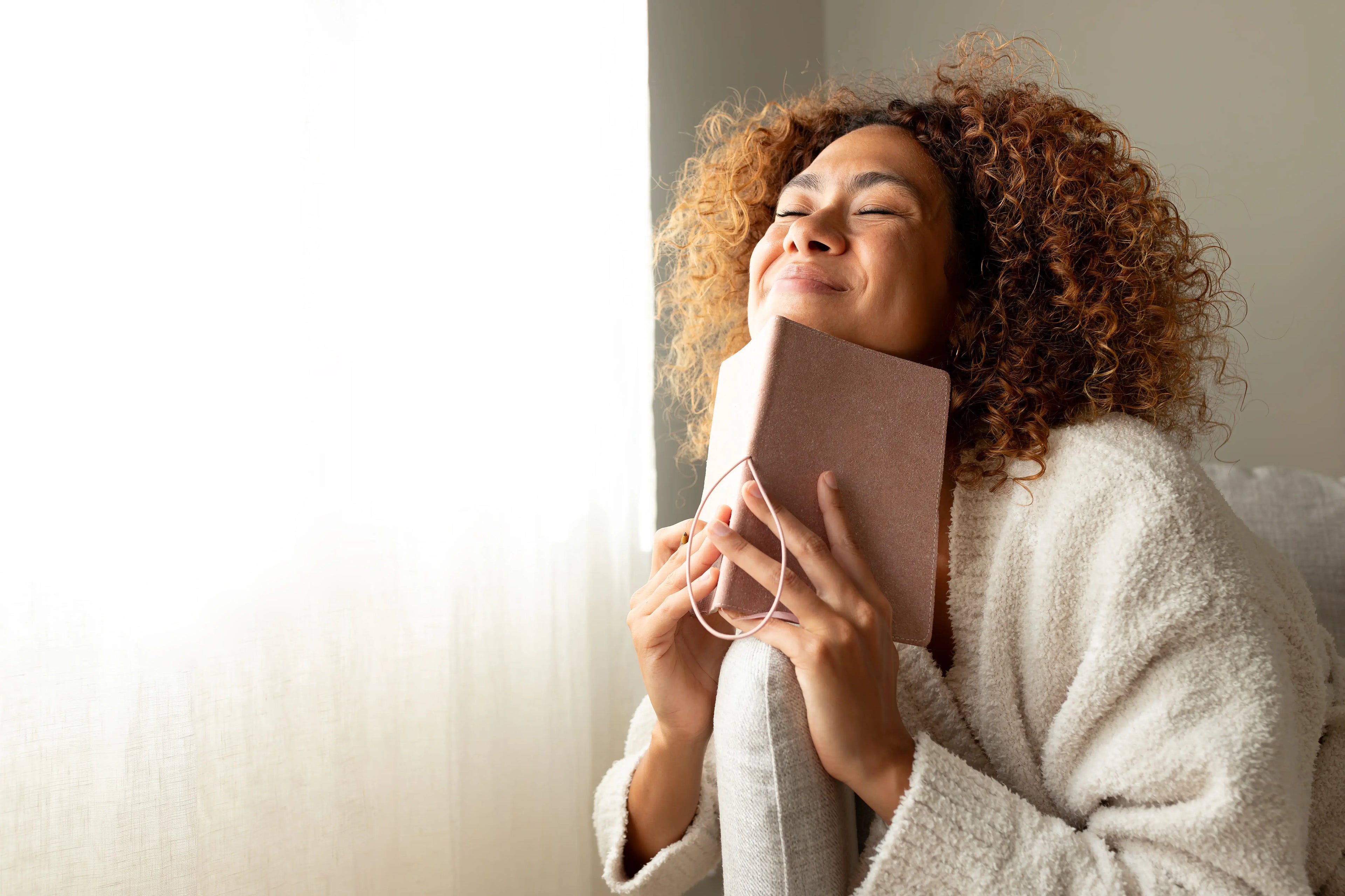 Woman smiling in a white cardigan holding a pink journal